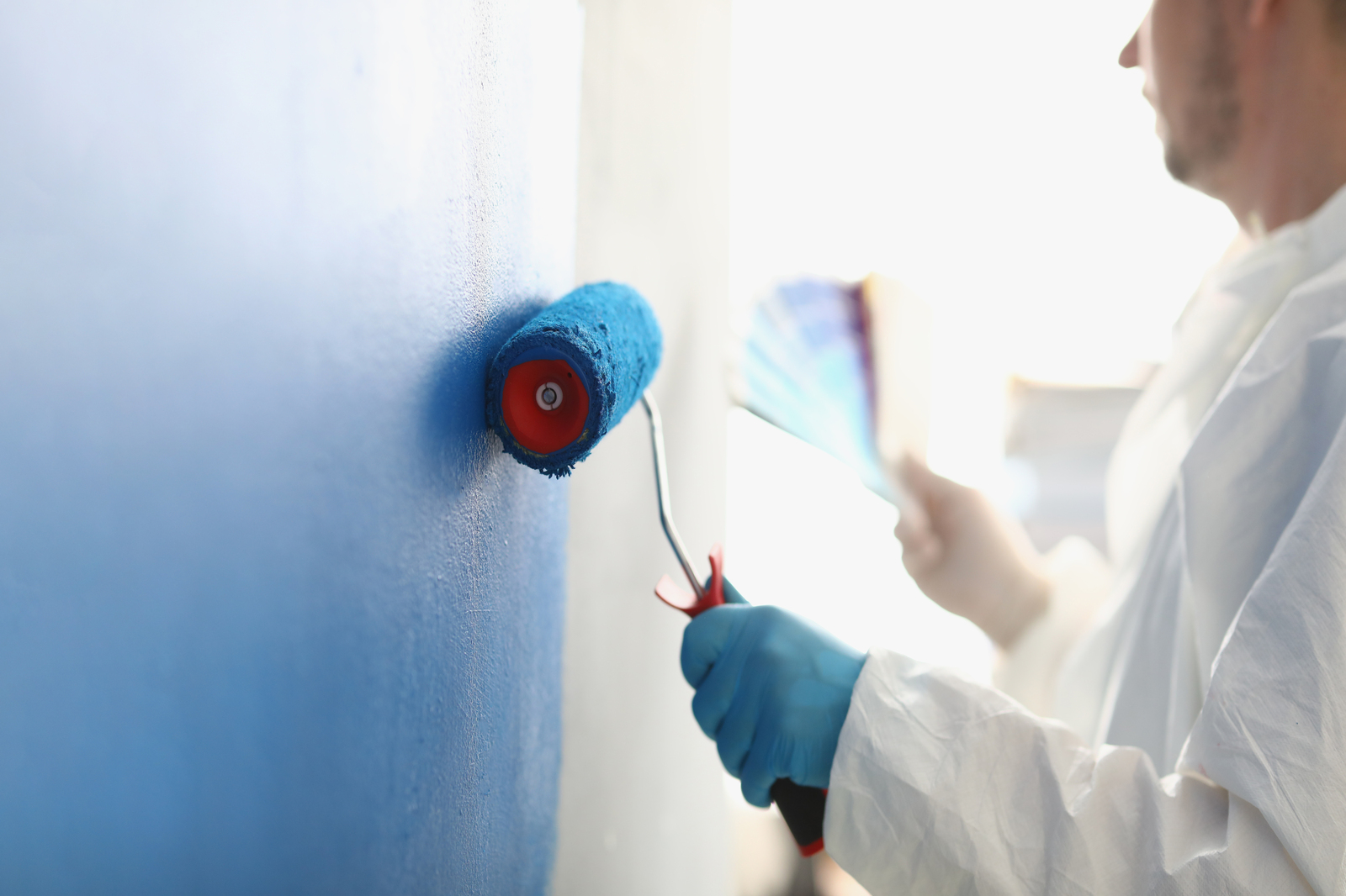 Painting white wall with blue roller. Services of master painter for home repair